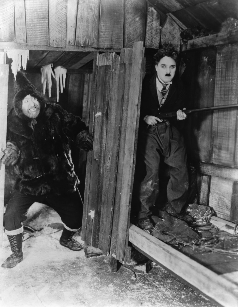 Chaplin,Mack Swain. Hallucinating from hunger, Big Jim decides to make a meal out of his companion.